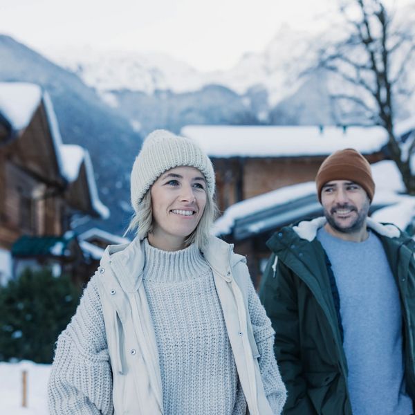 Ein Paar mit Winterbekleidung umarmt sich vor den Holz-Chalets im Feelfree Nature Resort im Winter